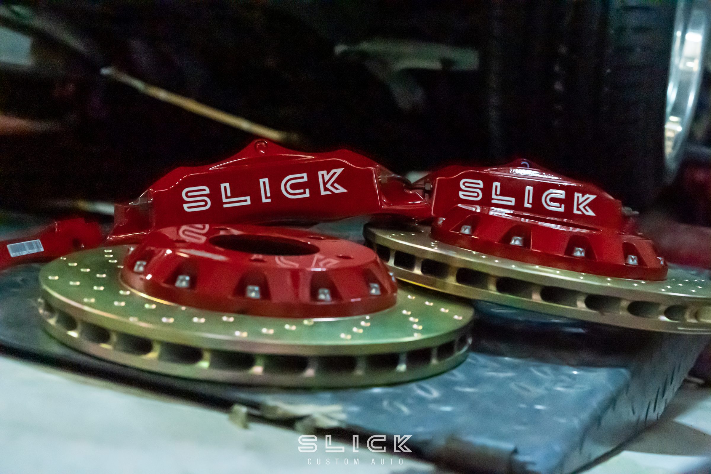 Slick-branded brake calipers and drilled discs on a workbench