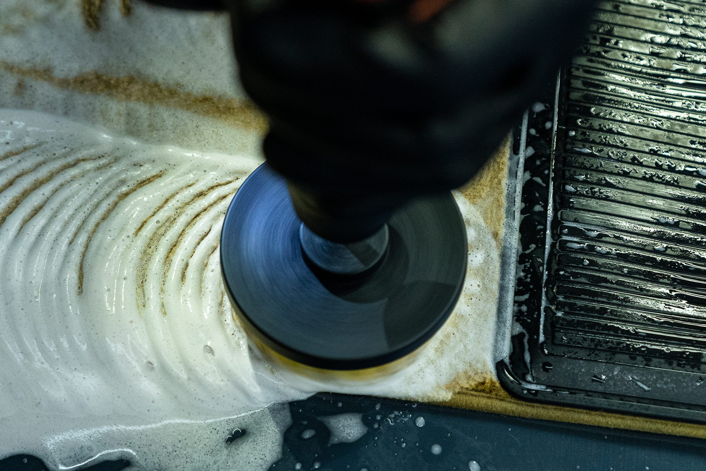 A machine polisher working a panel with polish spread across the paint