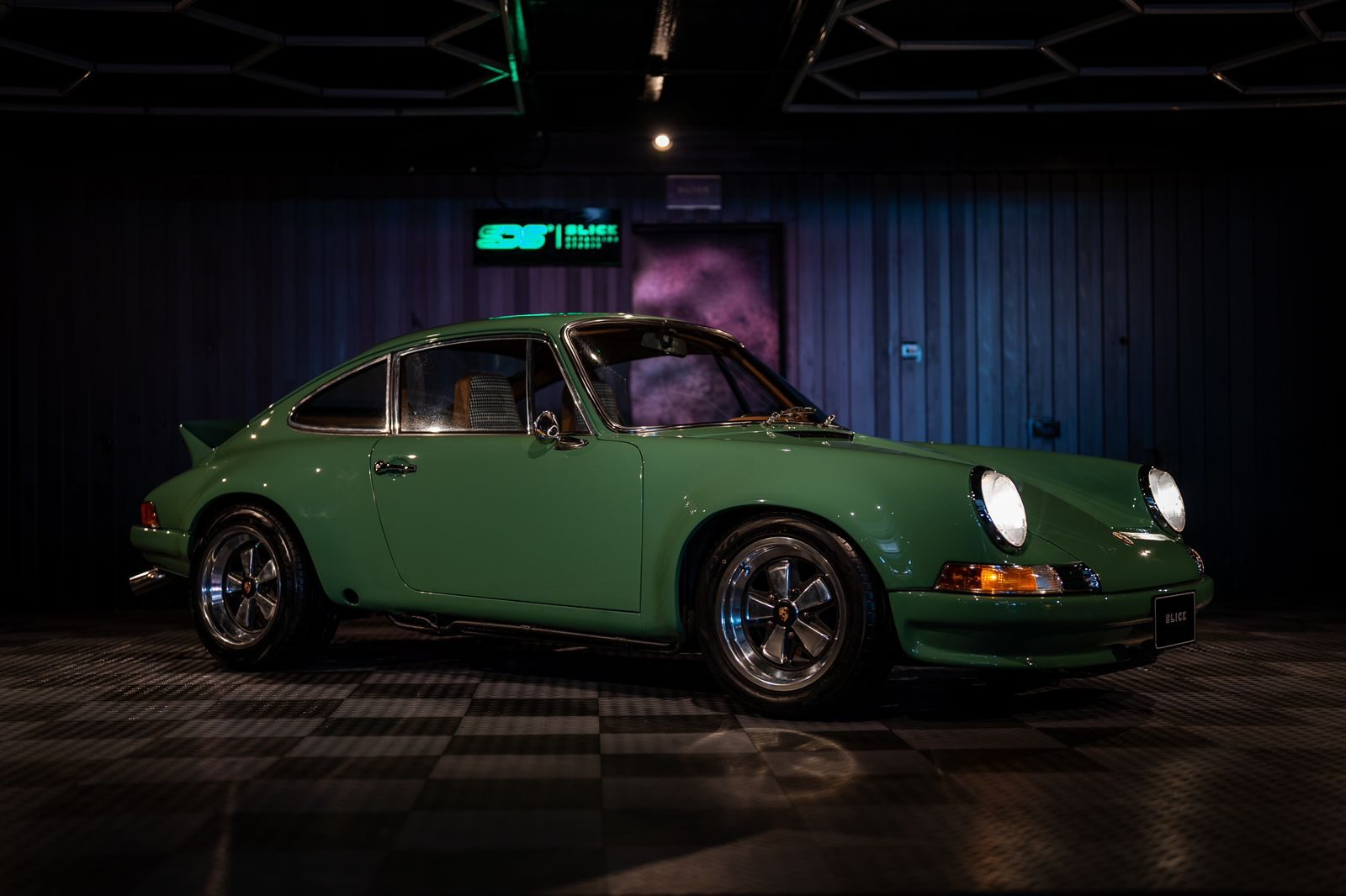 A green classic Porsche 911 in the dark detailing bay