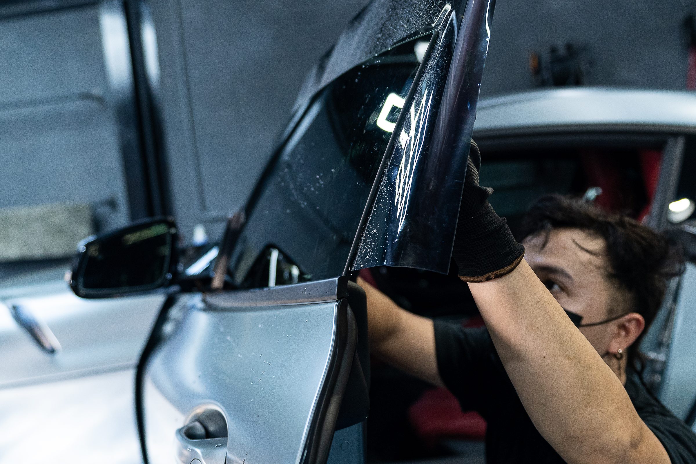 Window tint film being fitted to a door glass inside the detailing studio