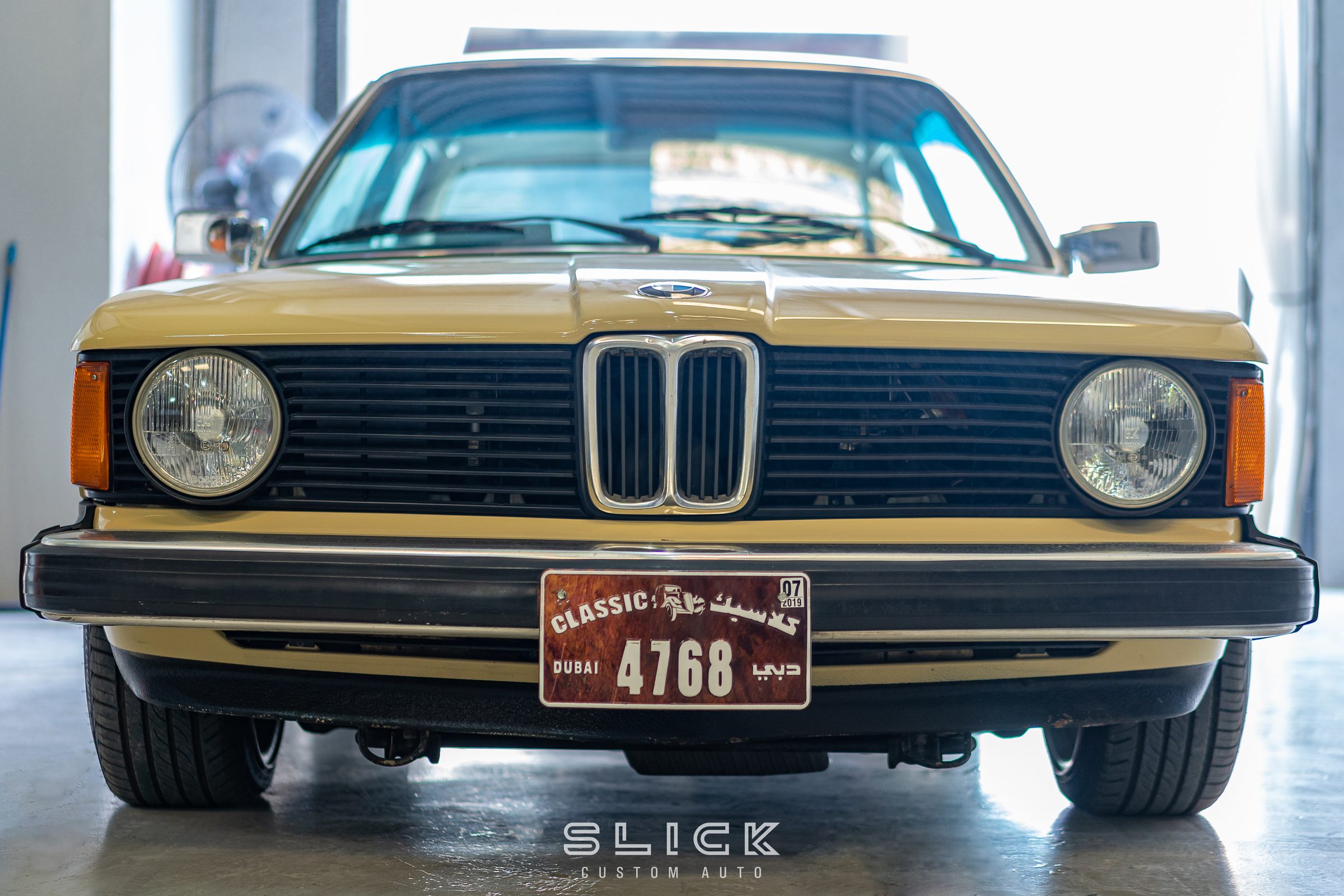 A restored gold classic BMW E21 photographed head-on
