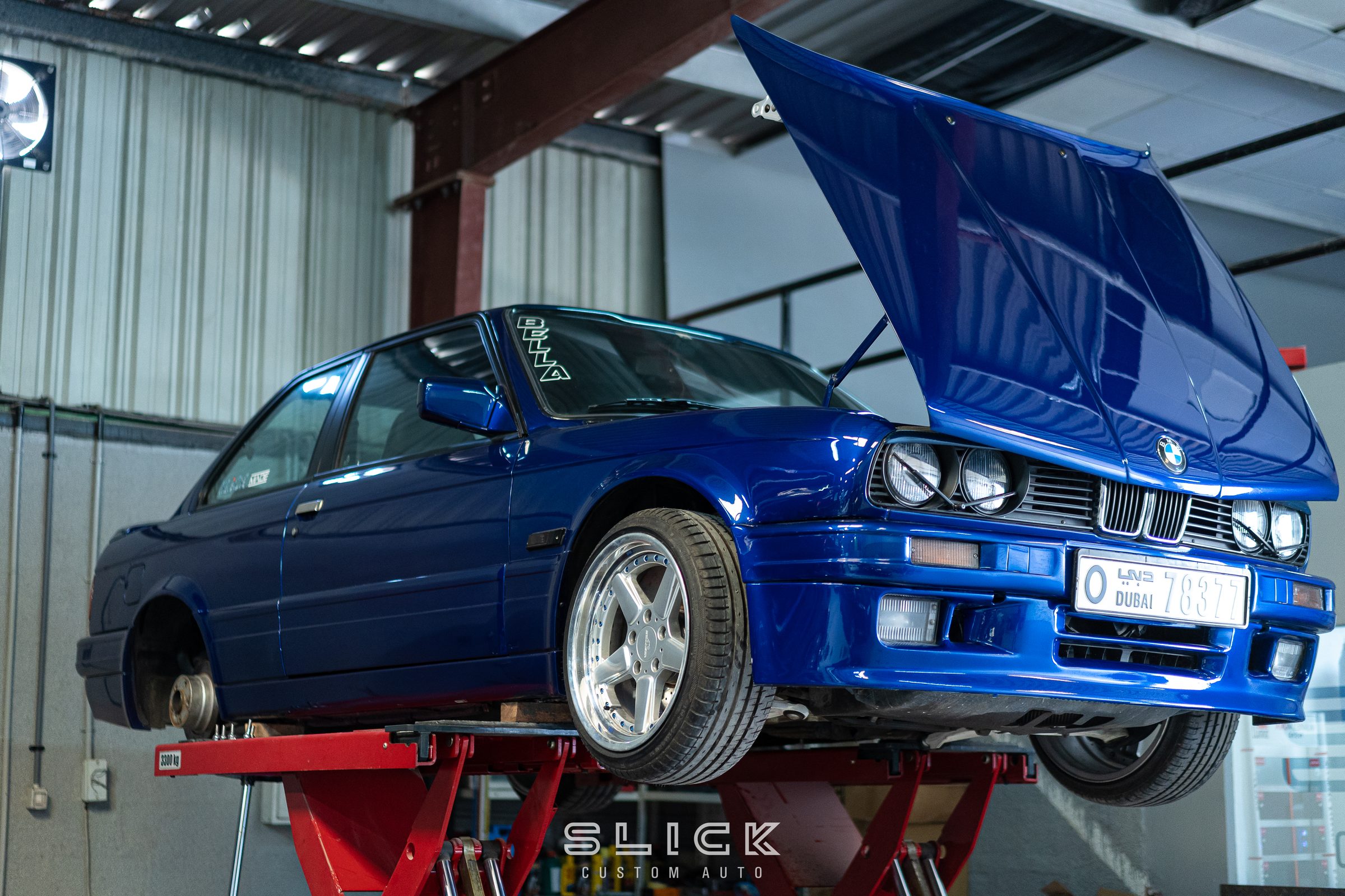 A blue classic BMW raised on a two-post lift with its bonnet open